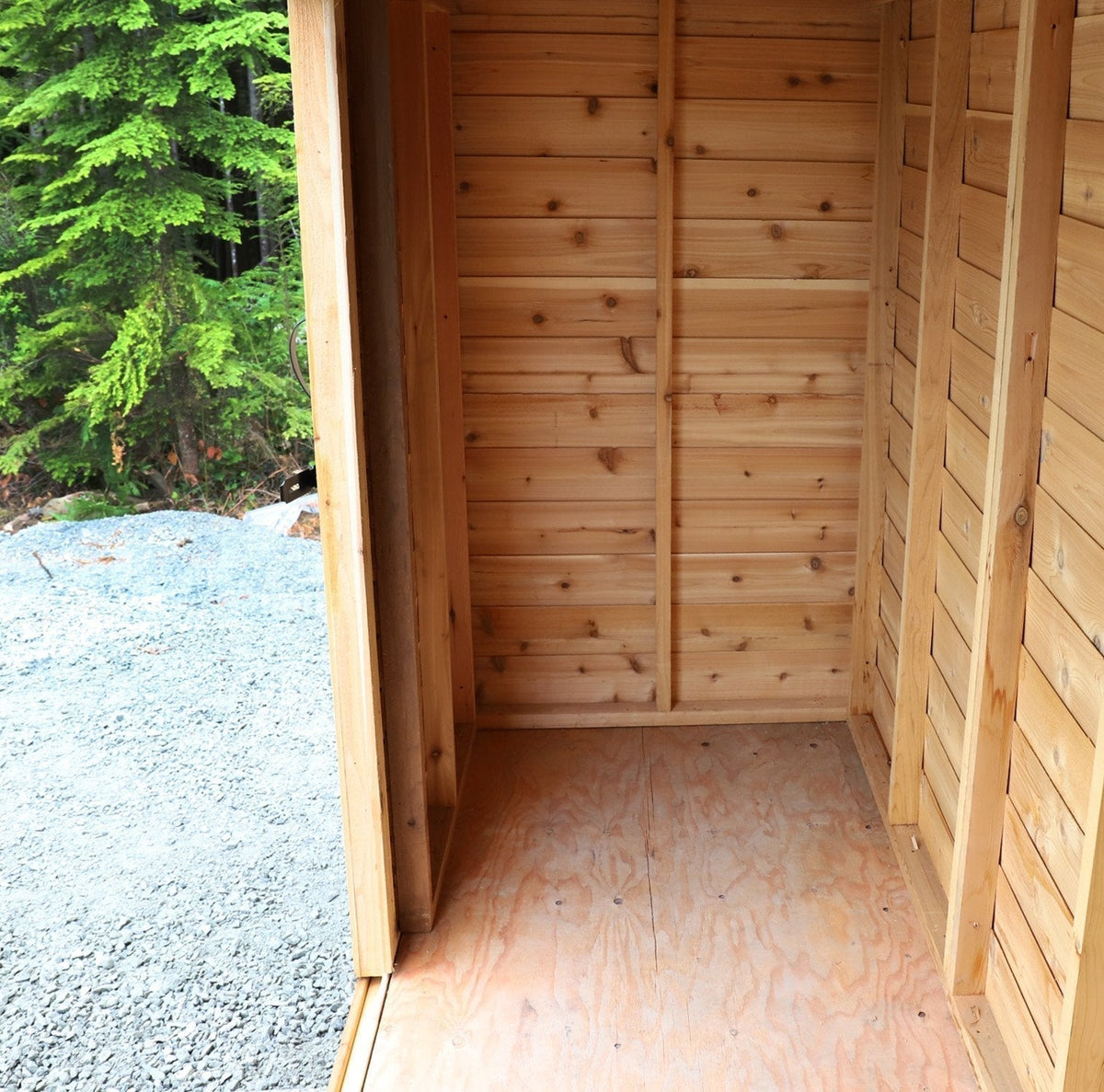 compact space cedar shed interior with natural wood walls, sliding doorway, and plywood floor