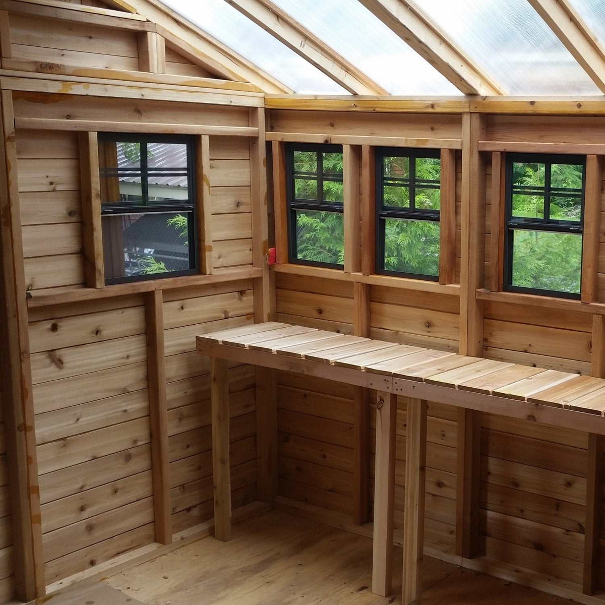 Cedar garden shed interior with natural wood walls, black-framed windows, translucent roof, and L-shaped workbench with Metal Roof